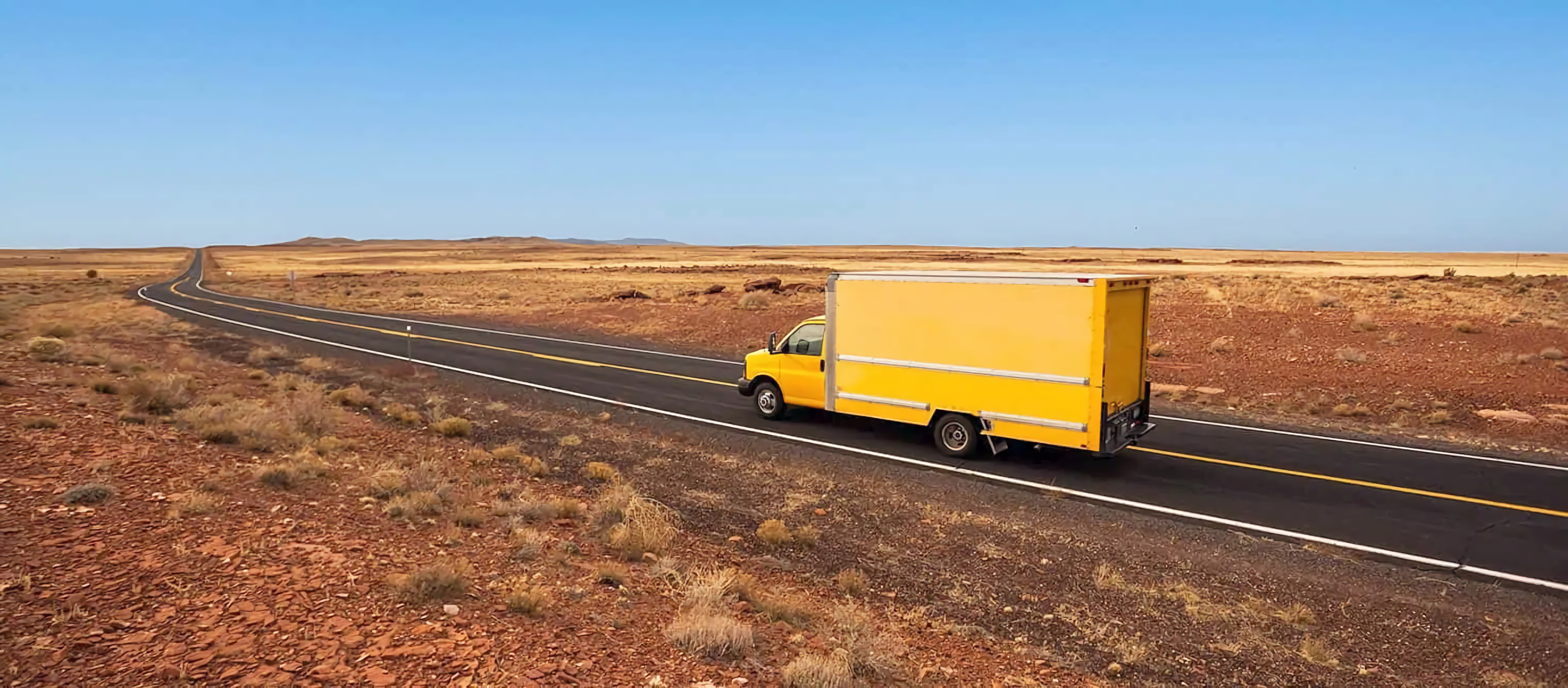 A yellow truck is driving cross country.